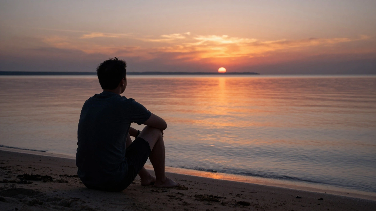 A solitary figure sitting on the beach at dusk, facing a mirror-like sunset reflection.
