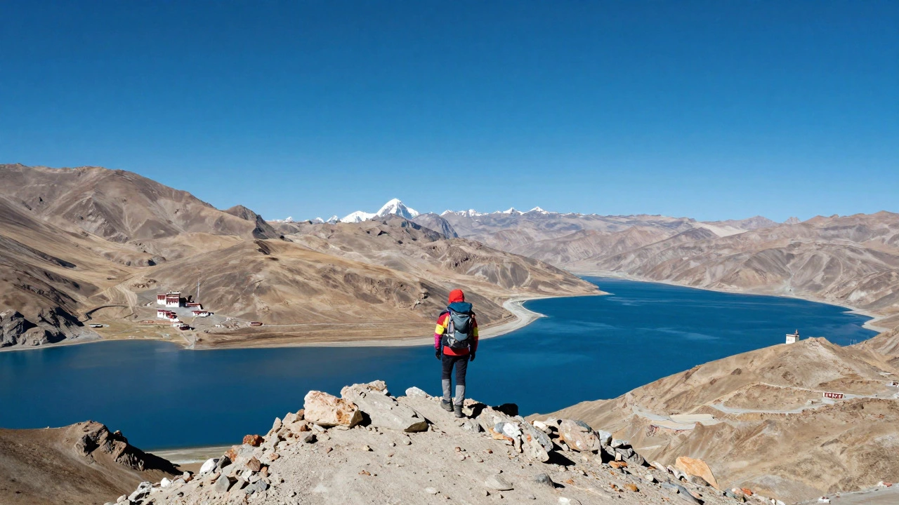 A trekker standing on a rocky ridge in Leh-Ladakh, India, overlooking a vast arid valley with a distant monastery under a clear blue sky.